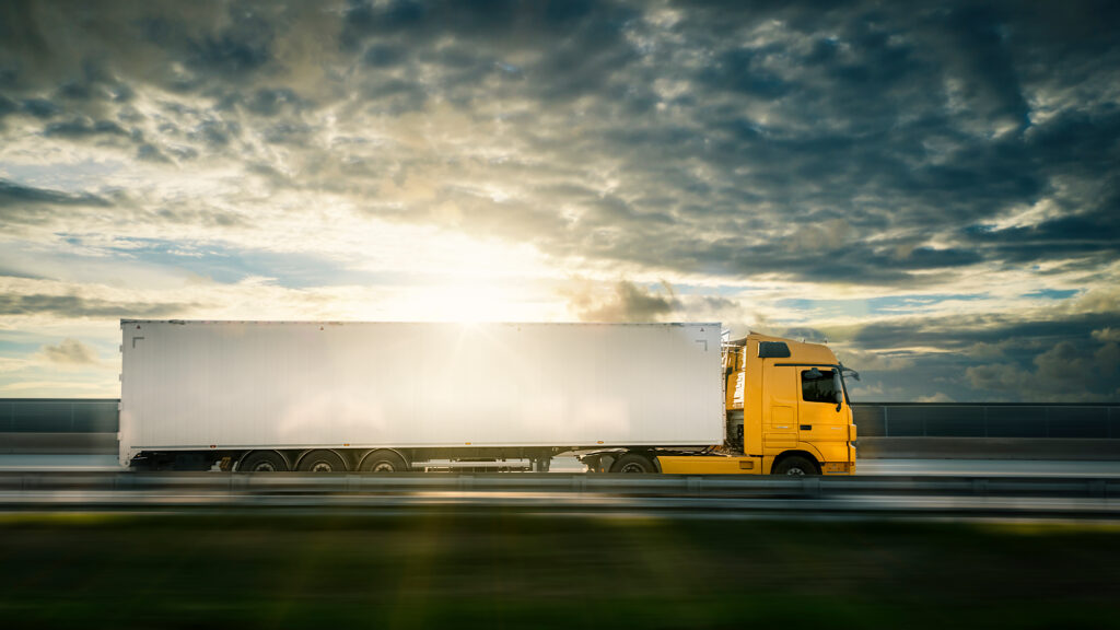 A semi truck travels down a highway as the sun dips below the horizon.